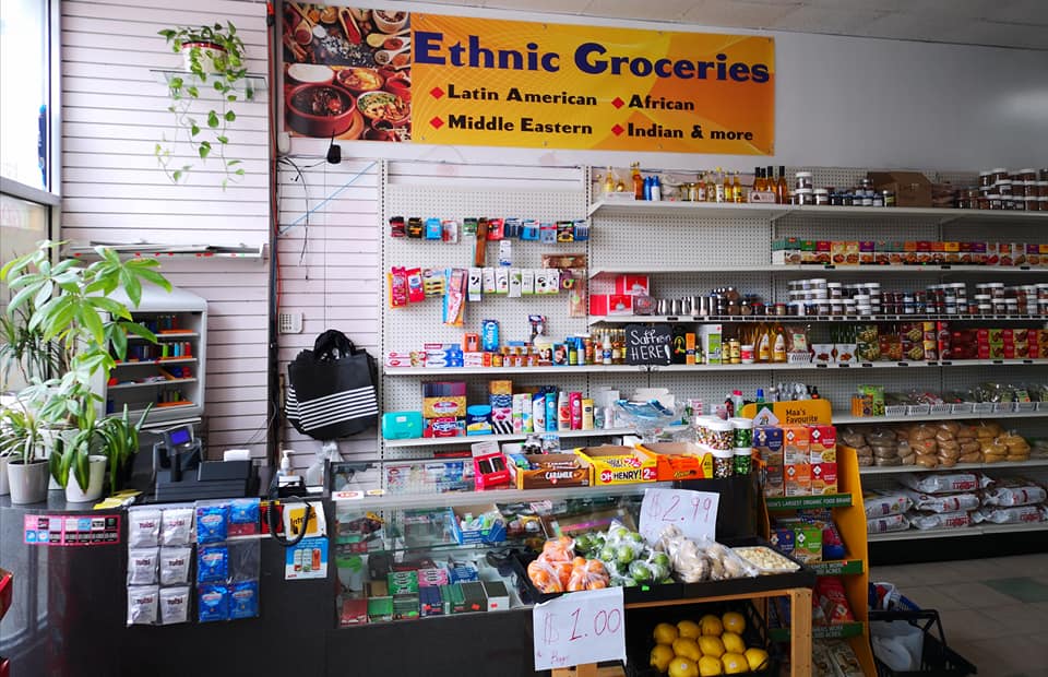 Interior of Goodies On Mews showing the register area with shelves of international products and the yellow Ethnic Groceries banner