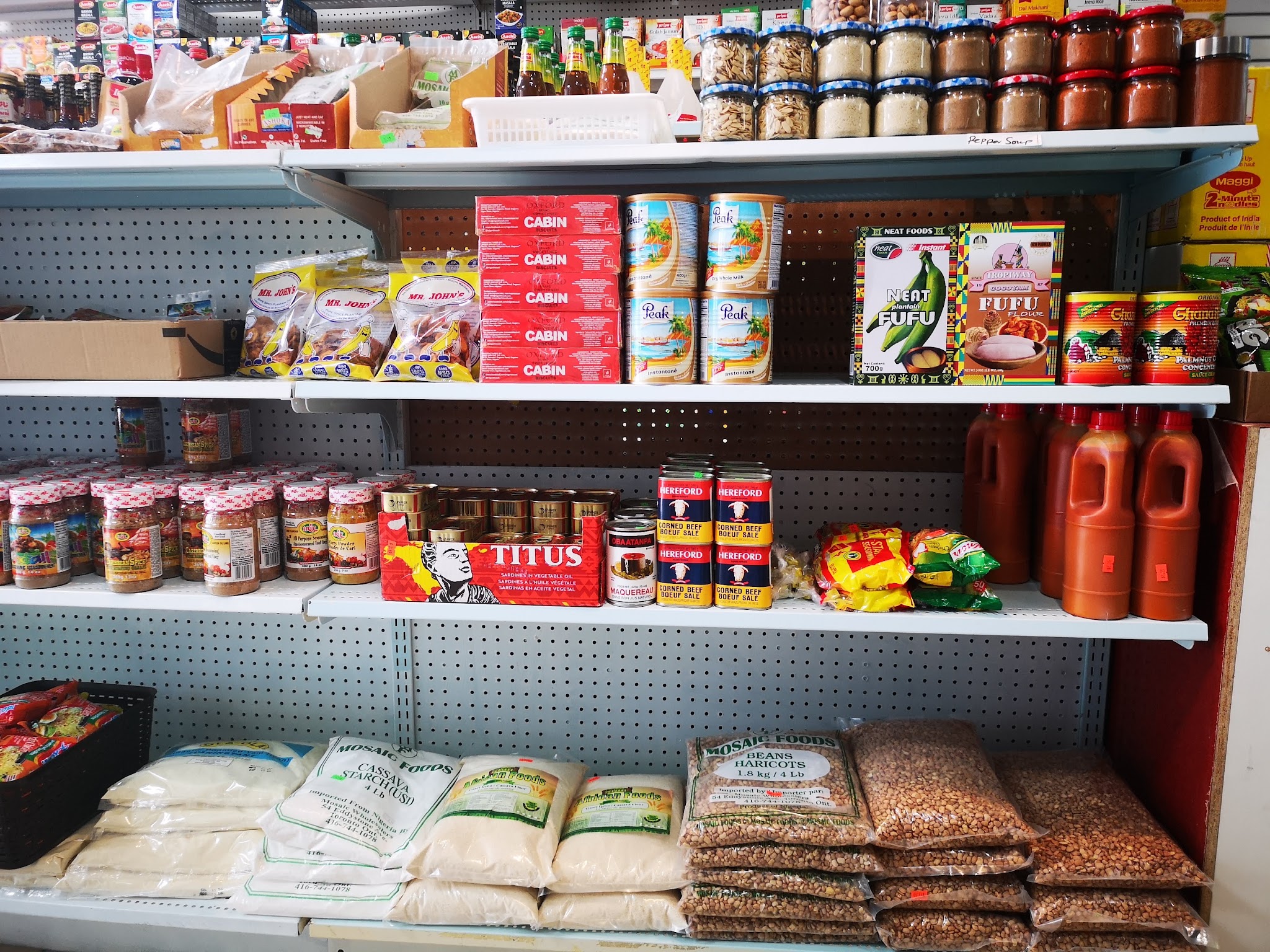 Shelves stocked with African grocery products including Titus sardines, Fufu flour, palm oil, Cabin biscuits, and cassava starch